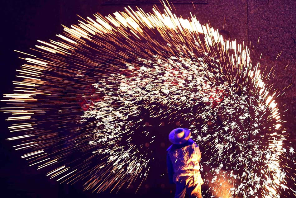 A folk artist performs the stunt of 'tree flowers' in Yu county in Hebei on Feb. 23, 2013. The stunt of "tree flowers" originated in Yu county. Blacksmith threw molten iron on the walls. The molten iron splashed radiance, forming 10,000 sparks, like a leafy canopy. It is called the "tree flower". (Xinhua/Chen Jianli)