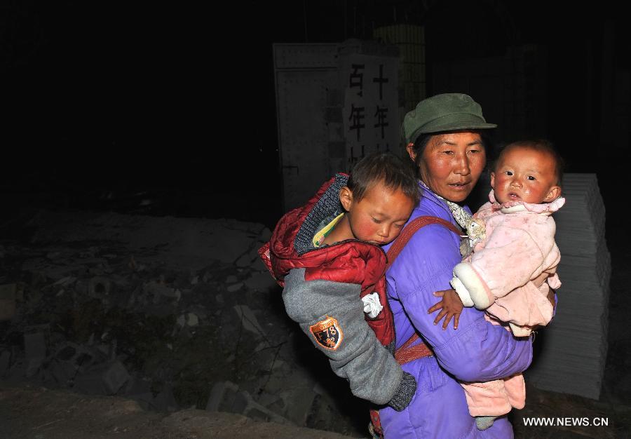 Local resident Yang Yuying carries her children as she walks past a piece of collapsed wall after a 5.5-magnitude earthquake in Eryuan County of Dali Bai Autonomous Prefecture, southwest China's Yunnan Province, on March 3, 2013. The number of people confirmed injured by a 5.5-magnitude earthquake that hit southwest China's Yunnan Province on Sunday afternoon has risen to 30, local authorities said. (Xinhua/Lin Yiguang) 