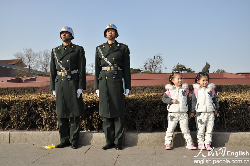 Two PLA soldiers are on duty at Tiananmen gate; and there are two twin sisters playing beside them on March 04, 2013.   (Photo/ People's Daily Online)