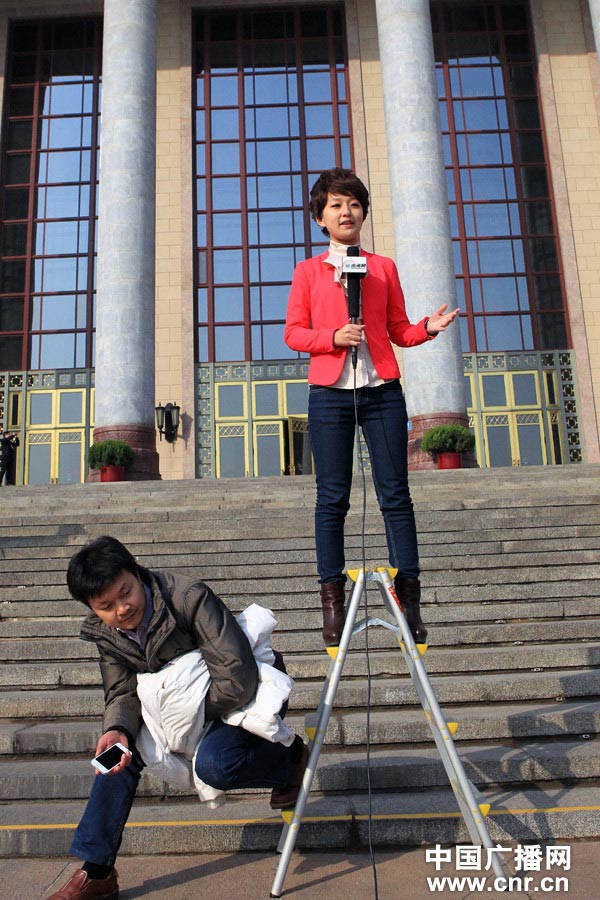 A television host wearing high heels stands on the ladder for better photo. (Photo/www.cnr.cn)