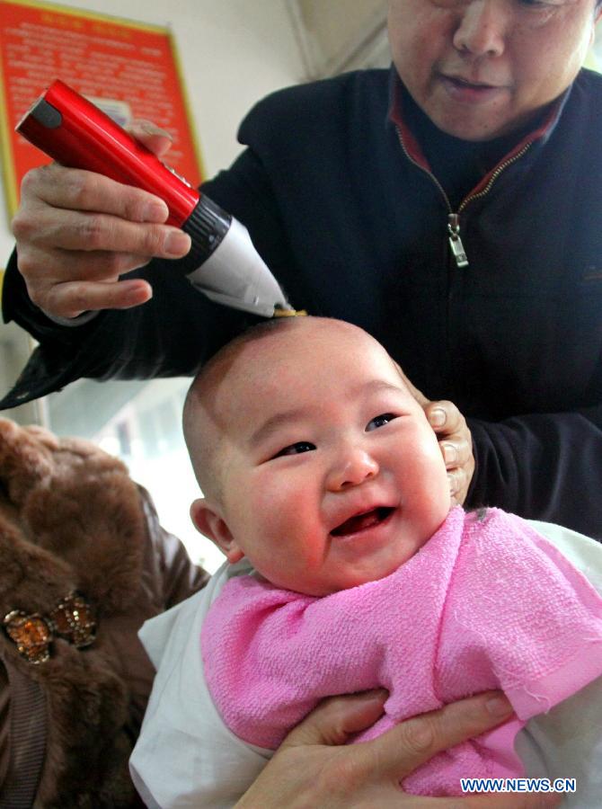 A baby smiles as having haircut at a barbershop in Shuangxi Township of Jiang'an County, east China's Jiangxi Province, March 13, 2013, on the occasion of the second day of the second lunar month, known in Chinese as Er Yue Er, "a time for the dragon to raise its head", as a Chinese saying goes. Barbershops across the country opened early to begin one of their busiest days of the year, as many Chinese hold the superstitious belief that getting a haircut at a time when the "dragon raises its head" means they will have a vigorous start to the new year. (Xinhua/Xu Zhongting)