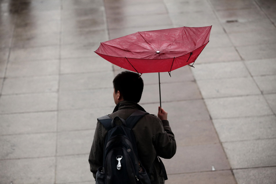 Wind blows a man’s umbrella inside-out at Tian’anmen Square on March 12. (Xinhua/ Jin Liwang)