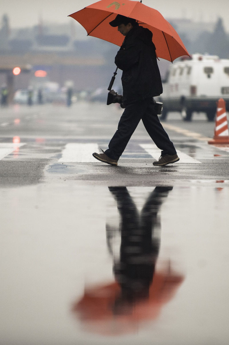 A journalist walks into Great Hall of the People regardless of the rain. The closing meeting of the first session of the 12th National Committee of the Chinese People's Political Consultative Conference (CPPCC) was held on Tuesday. On the same day, Beijing embraced the first spring rain in 2013. (Xinhua News Agency/Liu Jinhai)