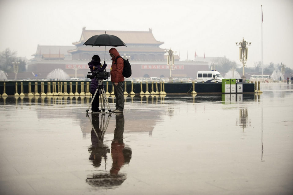Two journalists wait at the entrance in the rain. The closing meeting of the first session of the 12th National Committee of the Chinese People's Political Consultative Conference (CPPCC) was held on Tuesday. On the same day, Beijing embraced the first spring rain in 2013. (Xinhua News Agency/Liu Jinhai)