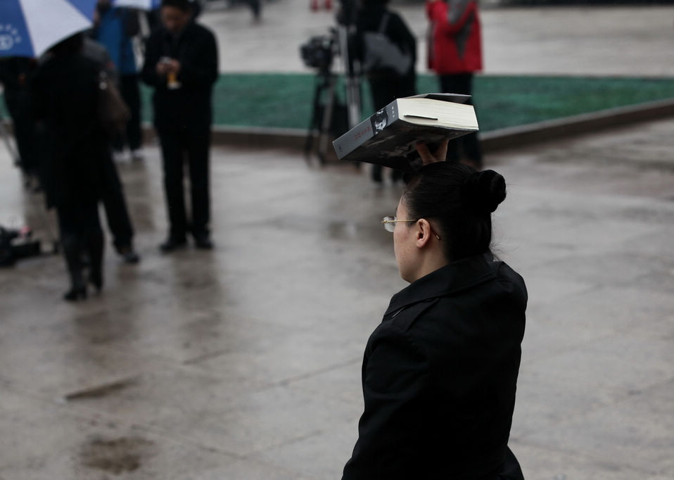 An attendee of CPPCC hides himself under a thick book to avoid the rain. The closing meeting of the first session of the 12th National Committee of the Chinese People's Political Consultative Conference (CPPCC) was held on Tuesday. On the same day, Beijing embraced the first spring rain in 2013. (Xinhua News Agency/Liu Jinhai)