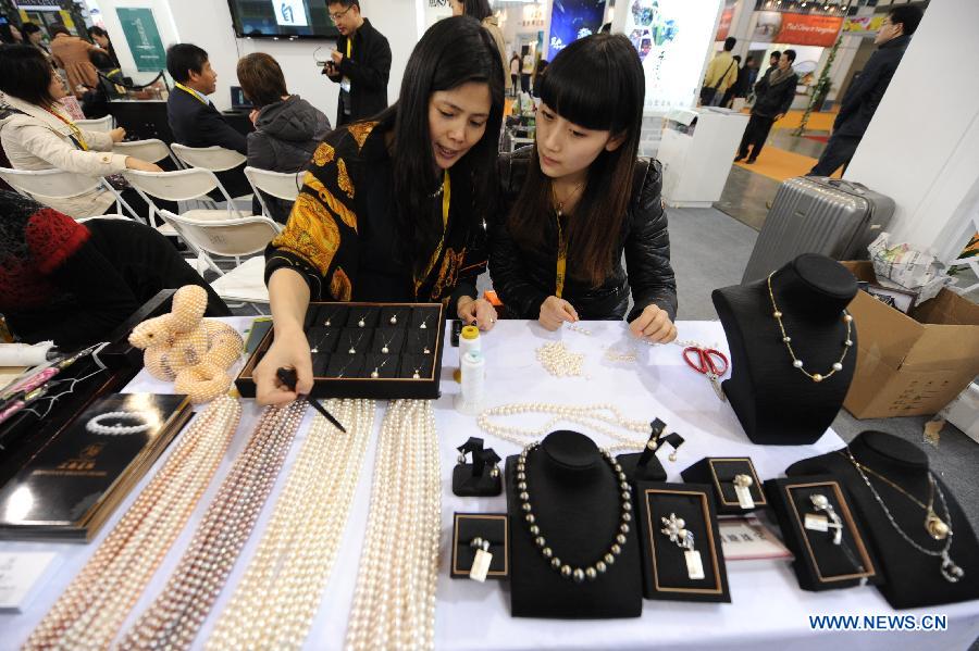 A staff member of an exhibitor shows a visitor how to make pearl accessories during the 2013 China International Exhibition for Caravanning, Motoring, Tourism (CMT China) in Nanjing, capital of east China's Jiangsu Province, March 15, 2013. The three-day exhibition, with the participation of 289 exhibitors from 28 countries and regions, opened in Nanjing Friday. (Xinhua/Shen Peng) 