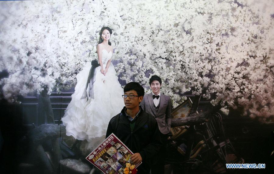 A man stands in front of a poster of wedding photo during the 2013 Xici Wedding Expo for Spring in Nanjing, capital of east China's Jiangsu Province, March 16, 2013. Most of the exhibitors possess both physical stores and online shops, attracting many net users to the expo which will last to March 17. (Xinhua/Yan Minhang)  