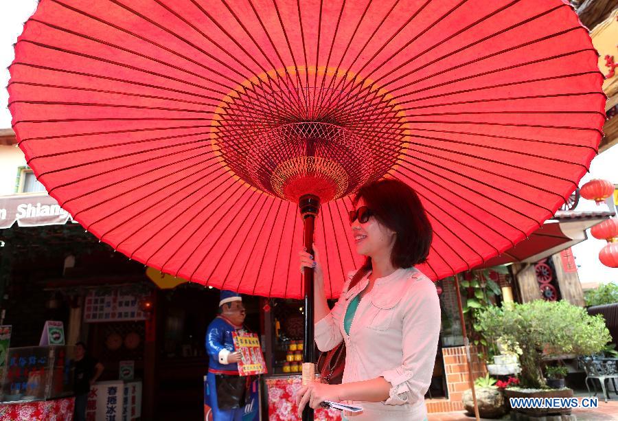 A girl holds a huge oil paper umbrella in Yuanxiangyuan Village of Kaohsiung City in southeast China's Taiwan, March 18, 2013. The Yuanxiangyuan Village has attracted a good many tourists thanks to its burgeoning oil paper umbrella industry. (Xinhua/Xie Xiudong)