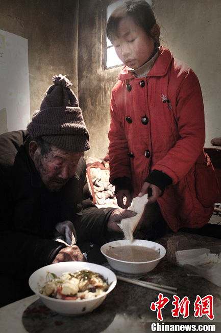 Song serves her grandfather with food- plain porridge, maize and fried kelps with eggs. (Chinanews.com / Zhou Panpan)