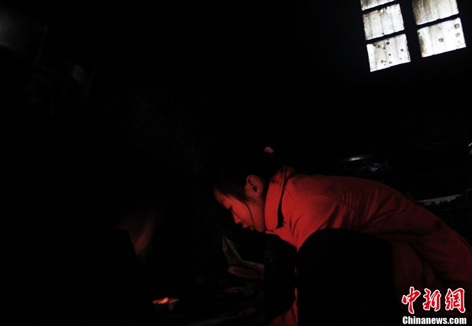 Song makes a fire to cook dinner in the dark. She saves every cent and does not put the light on. (Chinanews.com / Zhou Panpan)