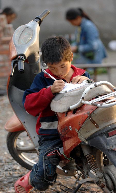 Wang Haodong, a student from Lantian Primary School, is fully concentrated on his homework whilst sitting on a motorbike parked in front of a waste disposal station under the Jiaxing Bridge on Oct. 26, 2008. He was born in Chengdu and his mother was a janitor. (Zhejiang Daily/Chu Yongzhi)