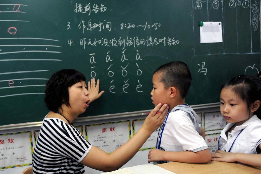A teacher corrects a student's pronunciation of the letter "o" inside a classroom of Junru Primary School on Aug. 11, 2009. Before the start of school, a great many primary schools had already opened their preschool departments for the purpose of adjusting the students to school life in advance. (Zhejiang Daily/Chu Yongzhi)
