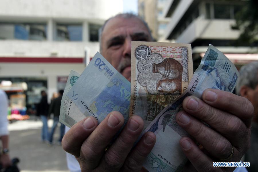 A Cypriot man shows Cypriot pound and euro banknotes in Nicosia March 25, 2013. Ordinary Cypriots are numb and worried on the aftermath of the new Eurogroup's agreement, which offers a harsh 10 billion euro bailout deal to Cyprus, including the radical reshaping of the Cypriot banking system. Depositors will lose a large portion of their money exceeding 100,000 euros in the bank. (Xinhua/Marios Lolos) 