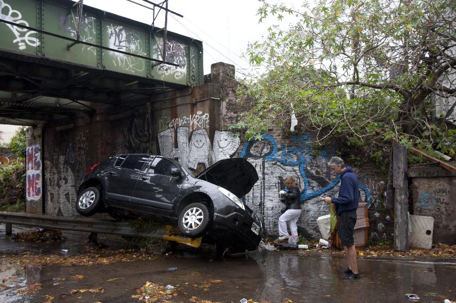 Residents walk in front of a vehicle damaged after a storm hit the city of Buenos Aires, capital of Argentina, on April 2, 2013. (Xinhua/Matín Zabala)  
