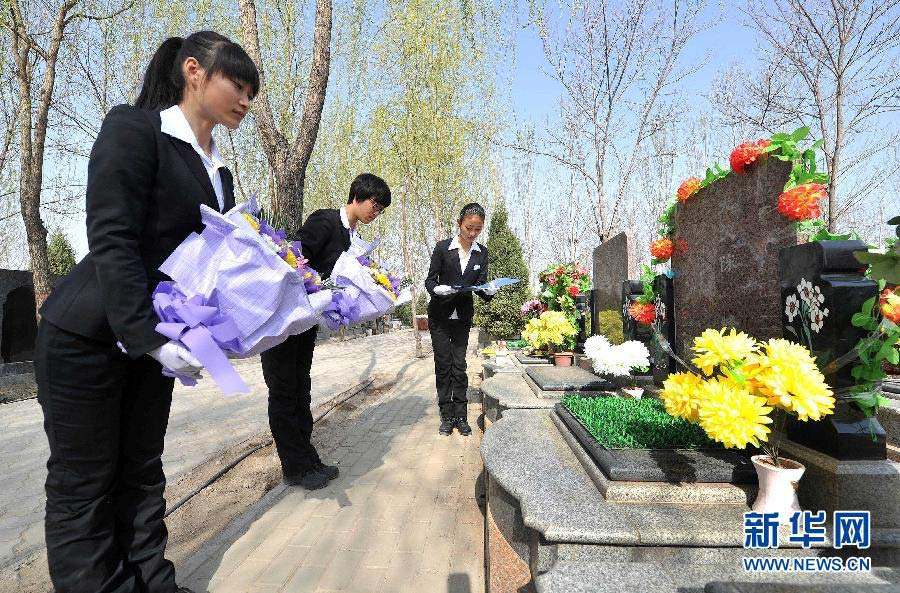 Funeral directors Lu Yufei (L) and Wang Na (C) hold flowers beside a tombstone as they pay respect to the dead in a cemetery in Yinchuan city, capital of Northwest China's Ningxia Hui autonomous region, on April 2, 2013. (Photo/Xinhua) 