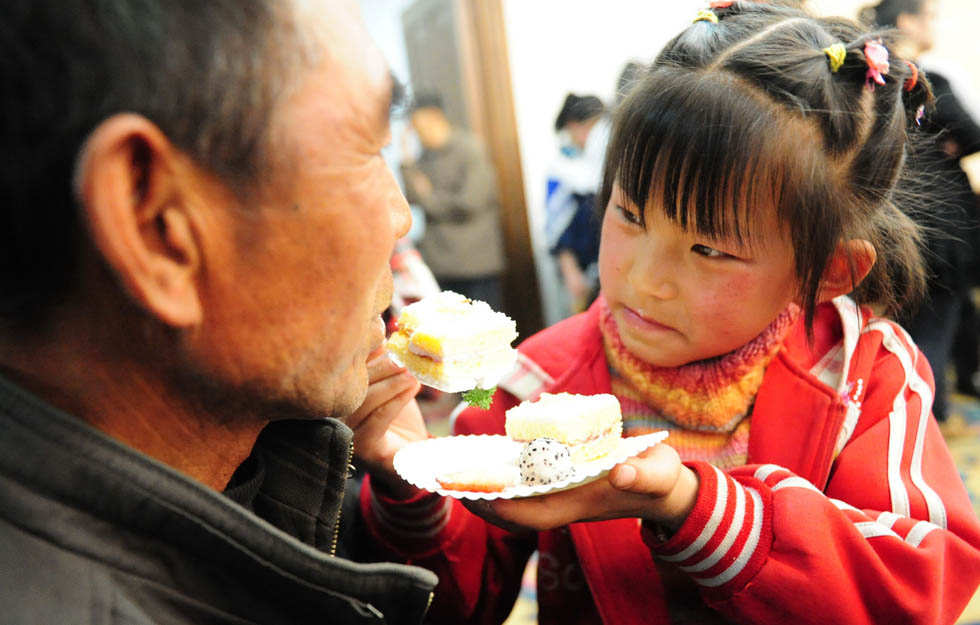 Liu Yumei (right) feeds her grandfather a piece of cake at a large-scale public welfare charity event held in Lanzhou.She was lucky to be funded to school. (Xinhua Photo/ Zhang Meng)