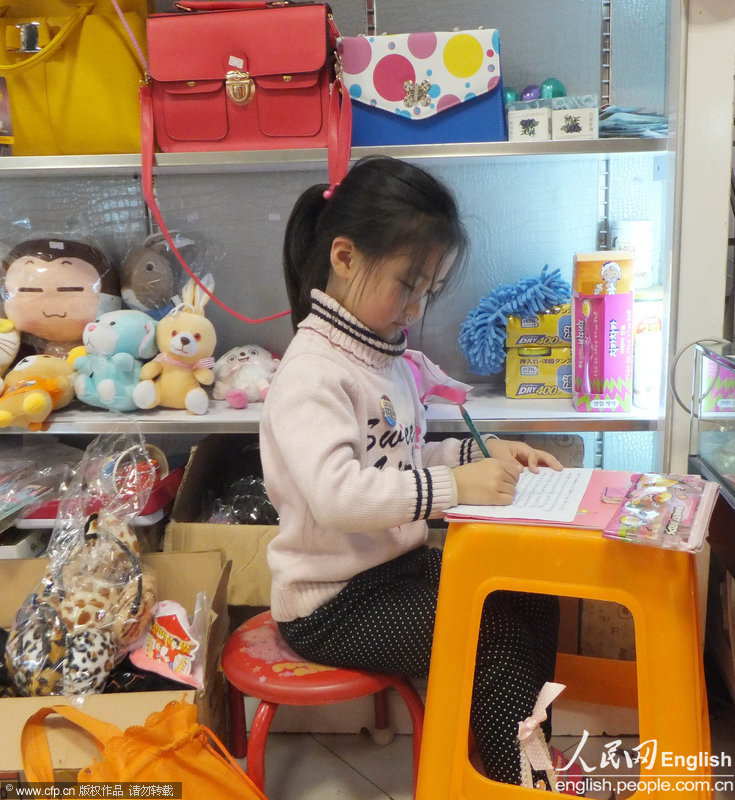 Tao Xiyi, 5, does her math homework on a plastic stool in her mother’s gift shop. (Photo by Wang Zhicheng/ CFP)