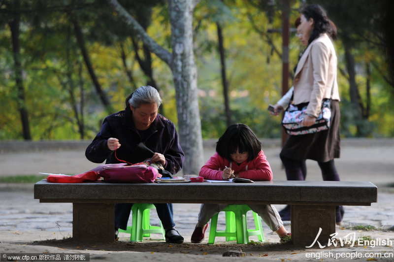 The girl in her second grade does her homework intently on a stone bench despite of passing visitors in Xi'an City Wall Park. Her mother knits a sweater next to her. (Photo/ CFP)