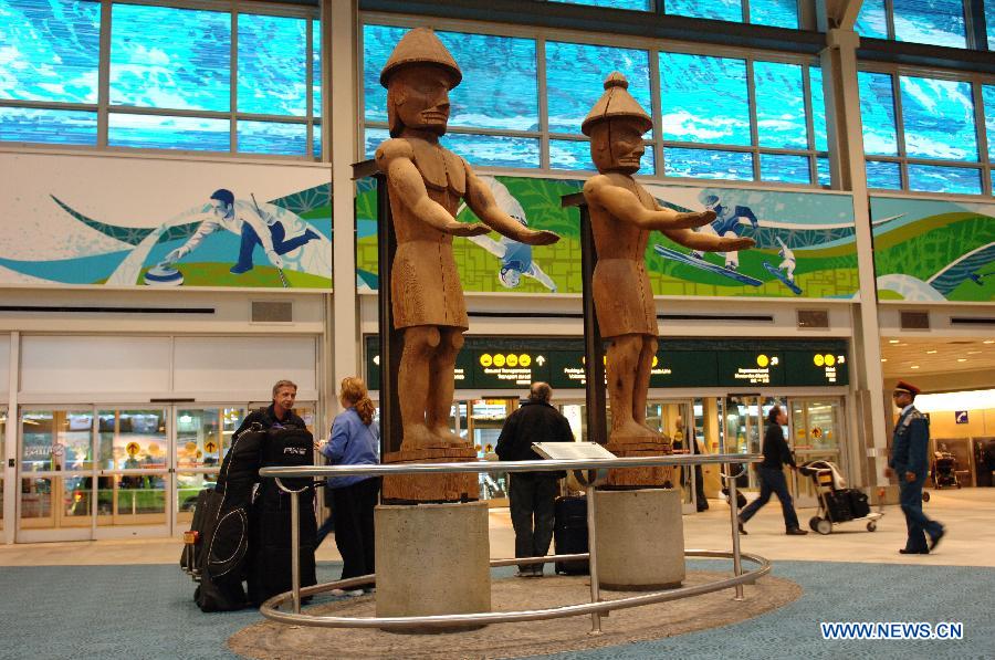 People walk past a wood carved sculptures entitled "The Welcome Figures" by Native Indian artist Joe David at Vancouver International Airport (YVR) in Vancouver, Canada, April 10, 2013. YVR was named Best Airport in North America at the Skytrax World Airport Awards in Geneva, Switzerland on April 10. YVR is rated 8th overall worldwide and is the only North American airport included in the top ten. (Xinhua/Sergei Bachlakov) 