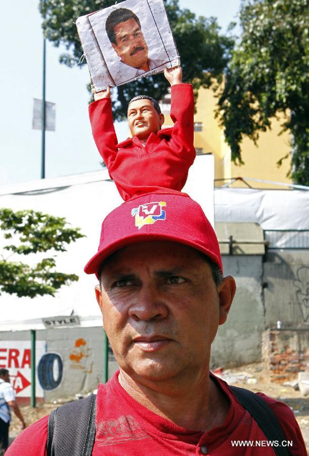 A resident wears a hat with a figure of the late Venezuelan president, Hugo Chavez, holding an image of the acting president and presidential candidate Nicolas Maduro, during Maduro's closing campaign, in the city of Caracas, capital of Venezuela, on April 11, 2013. (Xinhua/AVN) 