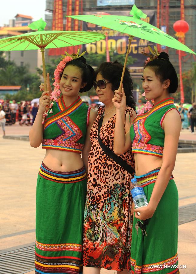A visitor poses for photo with girls of Dai ethnic group who perform a traditional umbrella dance to celebrate the Water Splashing Festival, also the New Year of the Dai ethnic group, in Jinghong City, Dai Autonomous Prefecture of Xishuangbanna, southwest China's Yunnan Province, April 14, 2013. (Xinhua/Qin Qing)