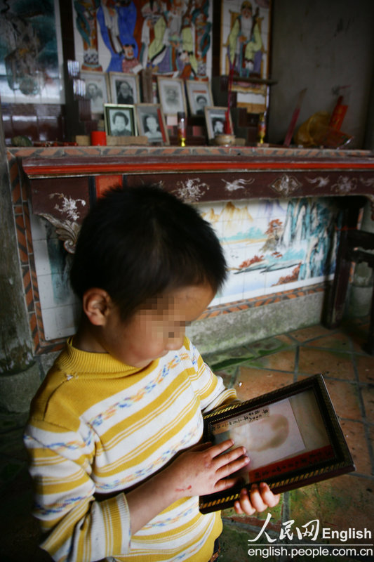 The younger son watches the only photo of his mother, April 4, 2013. There was a vague photo of the children' mother in the ancestral hall. Each time, when the children look at or touch the photo, they become very quiet. It contains the only and whole memory of the children for their dead mother. (CFP/Pan Deng)
