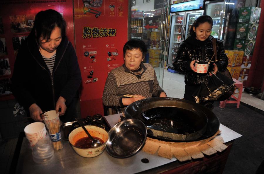 Peng Shuilin (M) and his wife (L) make fried tofu for customers. (Xinhua/ Li Ga)