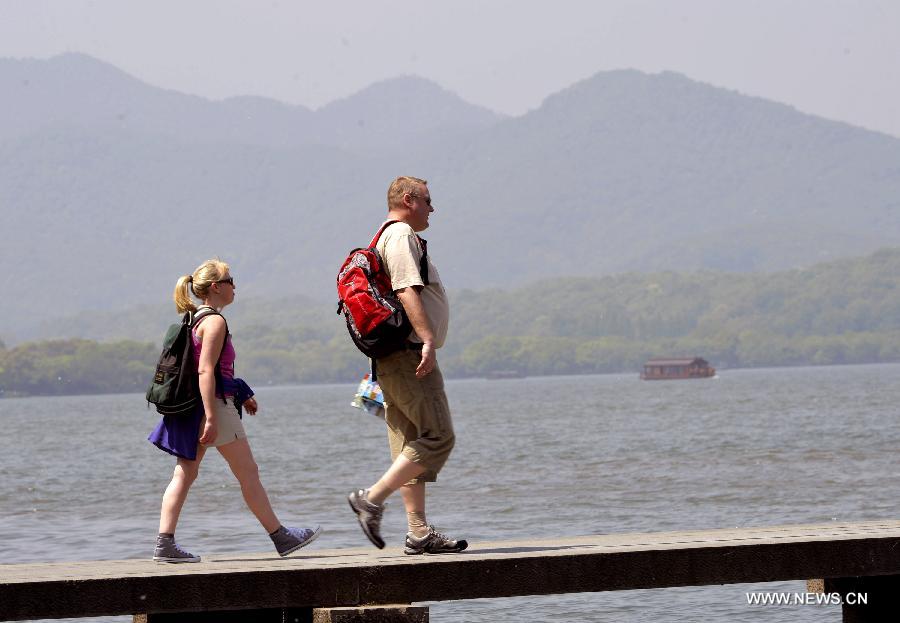 Foreign visitors in summer wear walk in Yongjin Park near the West Lake in Hangzhou, capital of east China's Zhejiang Province, April 15, 2013. The temperature in Hangzhou Monday approached 33 degrees Celsius, a record high at this time of year since 1951. (Xinhua/Shi Jianxue)