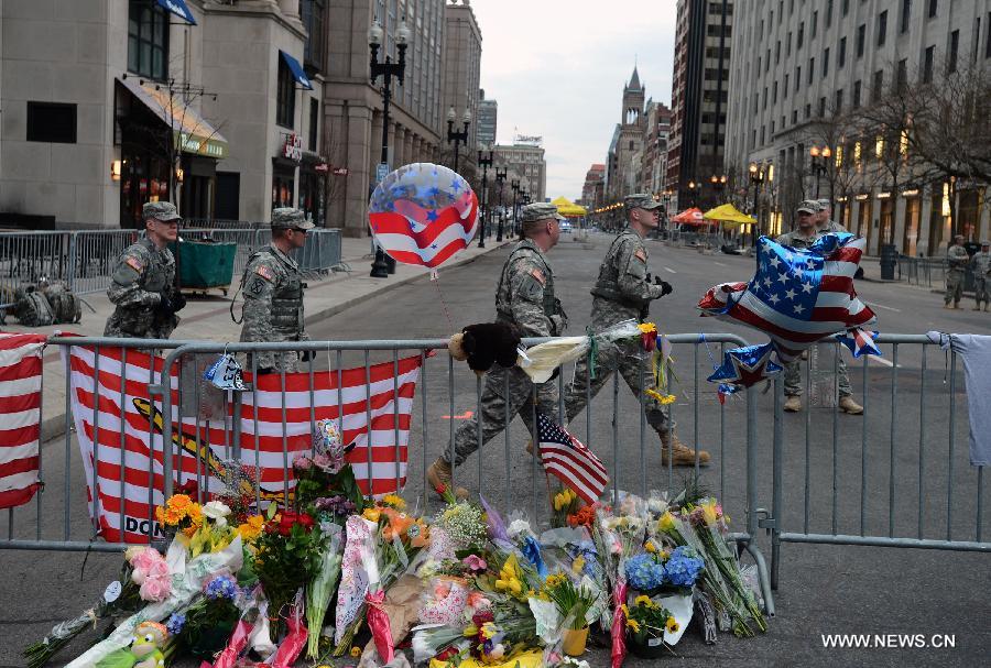 Soldiers walk past flowers for the victims in Boston Marathon blasts in Boston, the United States, April 16, 2013. The death toll has risen to three, with 176 people injured. (Xinhua/Wang Lei) 
