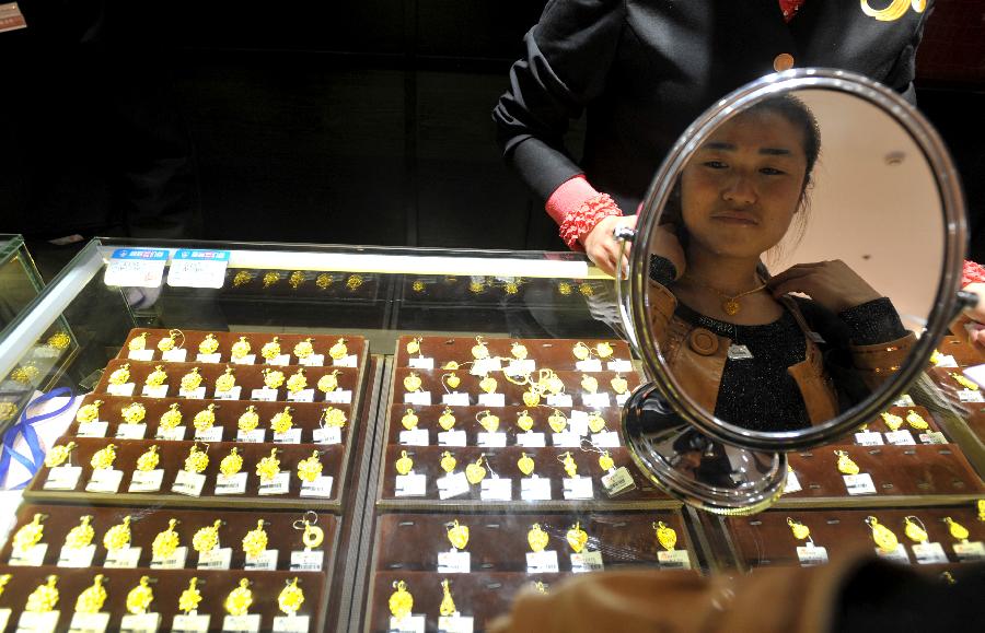 A consumer tries a gold necklace at a gold jewellery shop in Nanjing, capital of east China's Jiangsu Province, April 18, 2013. Gold jewellery shops through China have lowered price of gold jewellery due to the consecutive decline of gold price global markets recently, which boost sales in these shops. (Xinhua) 