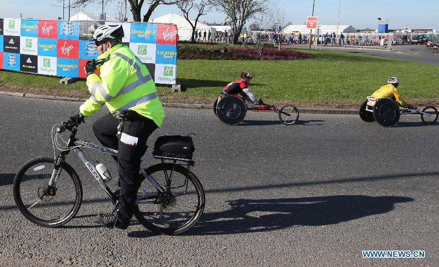 A policeman riding a bicycle passes athletes on wheelchairs during the London Marathon in Greenwich, London, capital of Britain, on April 21, 2013. (Xinhua/Yin Gang)