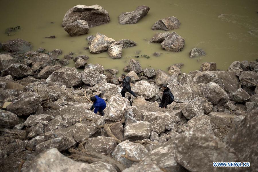 Residents try to pass through a road blocked by fallen rocks due to the landslide in the quake-hit Baosheng Township, Lushan County, southwest China's Sichuan Province, April 21, 2013. Baosheng Township is another seriously affected area in Lushan. Search and rescue work continued here Sunday, and the work for restoring roads and communications are conducted in the pipelines. (Xinhua/Fei Maohua)