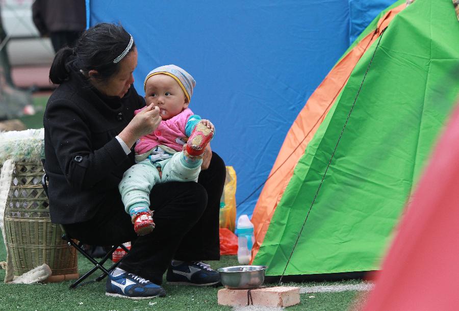 A woman feeds her grandson outside a tent at a temporary settlement in the quake-hit Baoxing County, southwest China's Sichuan Province, April 22, 2013. (Xinhua/Pei Xin)