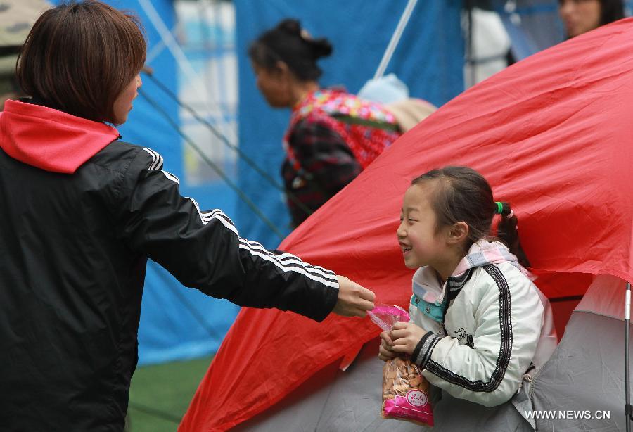 Gu Jingjing (R) takes a bag of snacks from her mother in the quake-hit Baoxing County, southwest China's Sichuan Province, April 22, 2013. (Xinhua/Pei Xin)