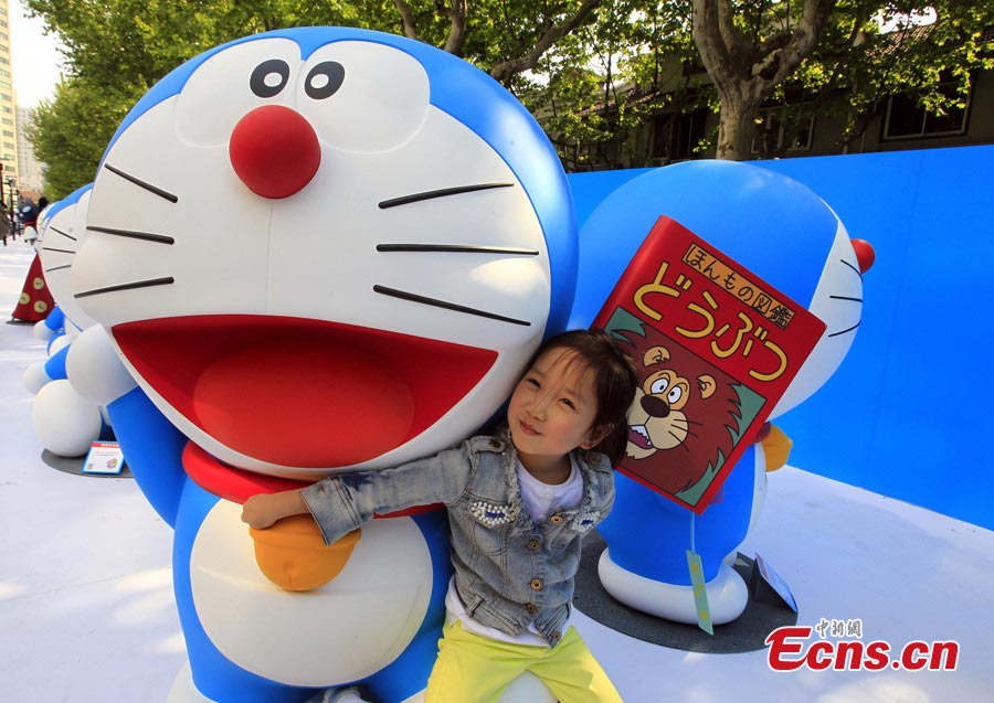 A girl poses with Doraemon, a robot cat in a Japanese animation series, at Xintiandi in Shanghai, April 26, 2013. An exhibition featuring 100 Doraemons with 100 different gadgets and machines it used in the series is being held at Xintiandi until June 16. It is the largest exhibition featuring Doraemon on the Chinese mainland. (CNS/Pan Suofei)