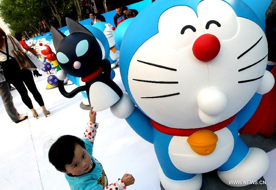 A boy plays with the Japanese a model of cartoon character Doraemon in Shanghai, east China, April 27, 2013. A total of 100 Doraemons models with different gestures and facial expressions were on display. (Xinhua/Chen Fei)