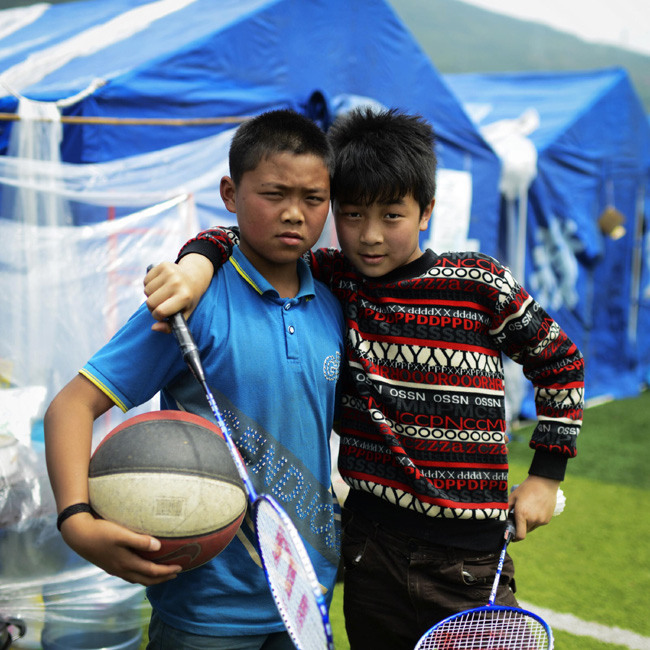 Sports fans Wu Zemin (L), 13, and Zhang Jie, 12, pose for a photo in a resettlement site for earthquake victims in Lushan county, Southwest China's Sichuan province. Photo taken on April 25. [Photo/Xinhua]