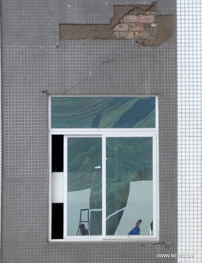 Workers building prefabricated houses are reflected on a piece of window glass of a teaching building destroyed in earthquake in Lushan County of Ya'an City, southwest China's Sichuan Province, April 30, 2013. The earthquake hitting Lushan on April 20 has damaged the buildings of 357 schools in Ya'an, disturbing the teaching activities in 329 middle and primary schools. Local people built prefabricated houses for the school children to continue their lessons in recent days. (Xinhua/Jin Liangkuai)