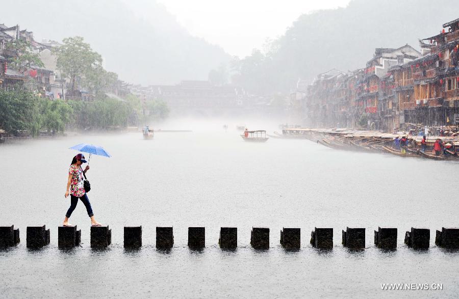 A tourist walks on rocks in Tuojiang River by the ancient town of Fenghuang in Fenghuang County of Xiangxi Tu and Miao Autonomous Prefecture, central China's Hunan Province, April 29, 2013. Fenghuang witnessed rainfall on Monday, the first day of the three-day Labor Day holiday. (Xinhua/Zhao Zhongzhi)