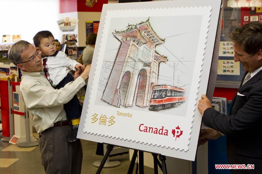 Illustrator Albert Ng (L) unveils one of the Chinatown Gates stamps with his grandson at a post office in Toronto, Canada, May 1, 2013. Canada Post launched a special series of stamps featuring Chinatown gates located in eight cities across the country on Wednesday to highlight the longstanding heritages of Chinese-Canadians. (Xinhua/Zou Zheng)