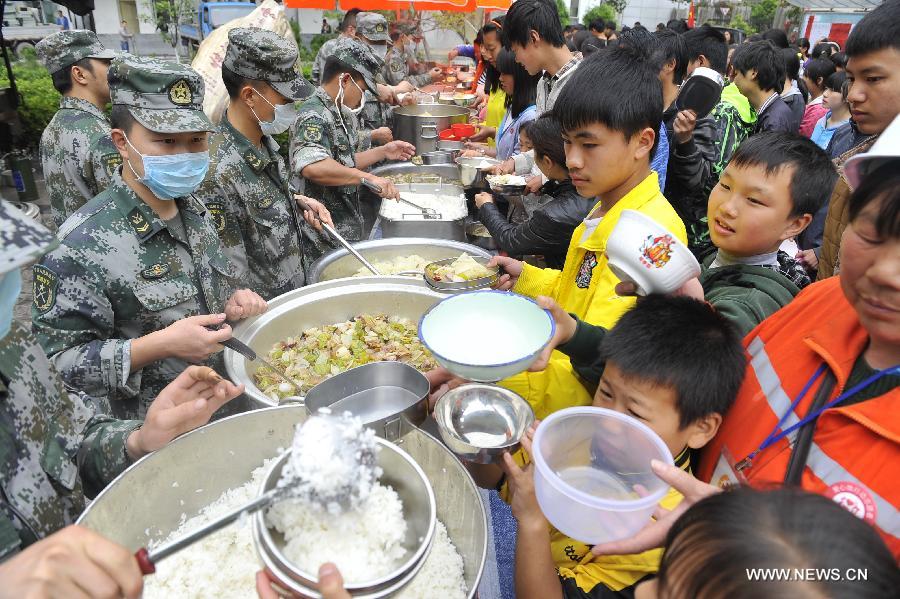 Soldiers distribute food for students at a school served as an evacuation settlement for displaced people in the quake-hit Baoxing County, southwest China's Sichuan Province, May 2, 2013. Some 4,000 displaced people live in the settlement, the largest in the county, after a strong earthquake hit Baoxing last month. At present, basic living needs of those people could be guaranteed in terms of food, drink, healthcare service and power supply. (Xinhua/Lu Peng)