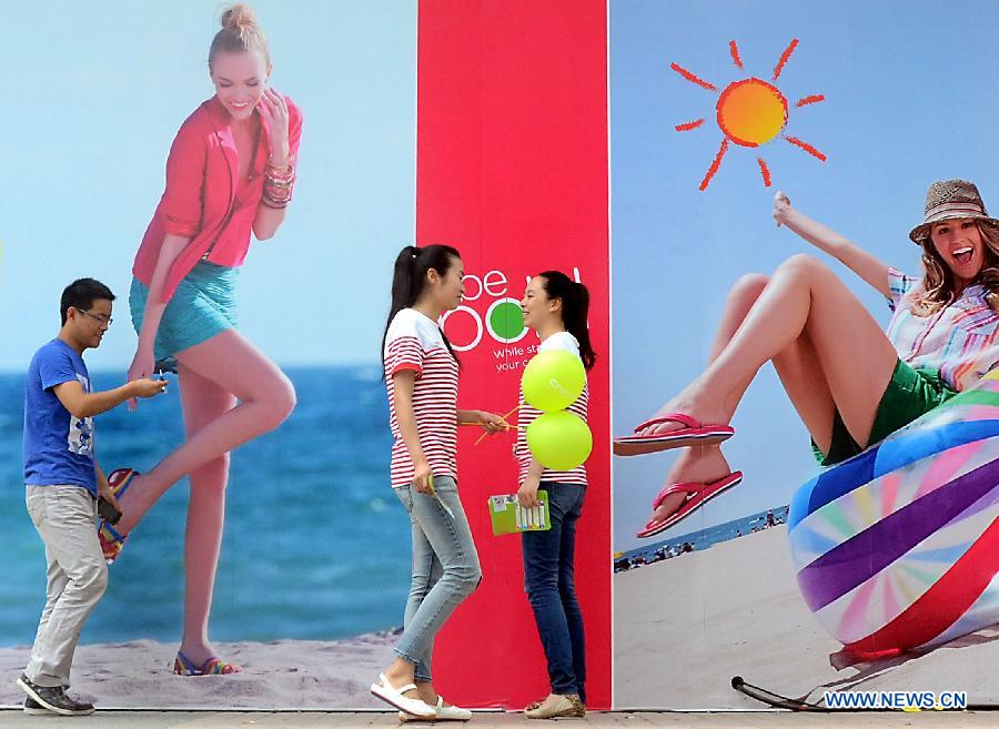 Young people wearing summer clothing walk past an advertisement board in Zhengzhou, capital of central China's Henan Province, May 5, 2013. Sunday is the beginning of the 7th solar term in Chinese lunar calendar, which indicates the coming of summer. The temperature in Henan rebounded in recent days. (Xinhua/Wang Song)