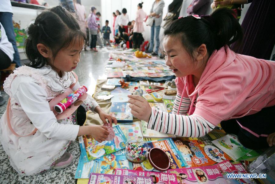 A girl (R) gives a gift to a buyer who has bought her book at the secondhand book fair in Nanjing, capital of east China's Jiangsu Province, May 5, 2013. During the fair, pupils and middle school students could sell or exchange their idle books, stationery and toys as well, by which they were expected by the organizer to learn a frugal lifestyle. (Xinhua/Wang Xin)