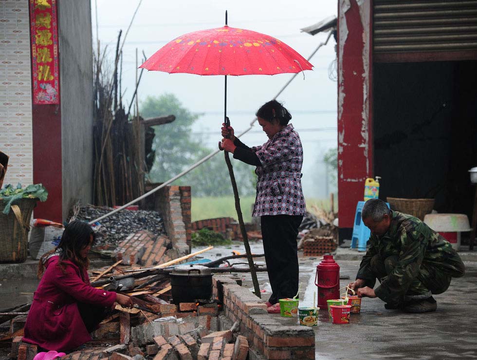 An old lady holds an umbrella for her family members who are cooking despite of rain in Lushan, Sichuan province. A 7.0-magnitude earthquake struck the county on April 20, leaving many people dead and injured. Photo taken by He Haiyang and released by Xinhua on April 28, 2013.