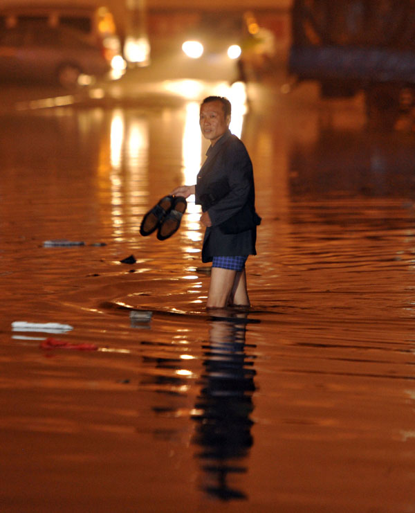 A passenger takes off his shoes and wades through the rain-drenched street in Changsha, capital of Central China's Hunan province on May 7, 2013. [Photo /Xinhua]