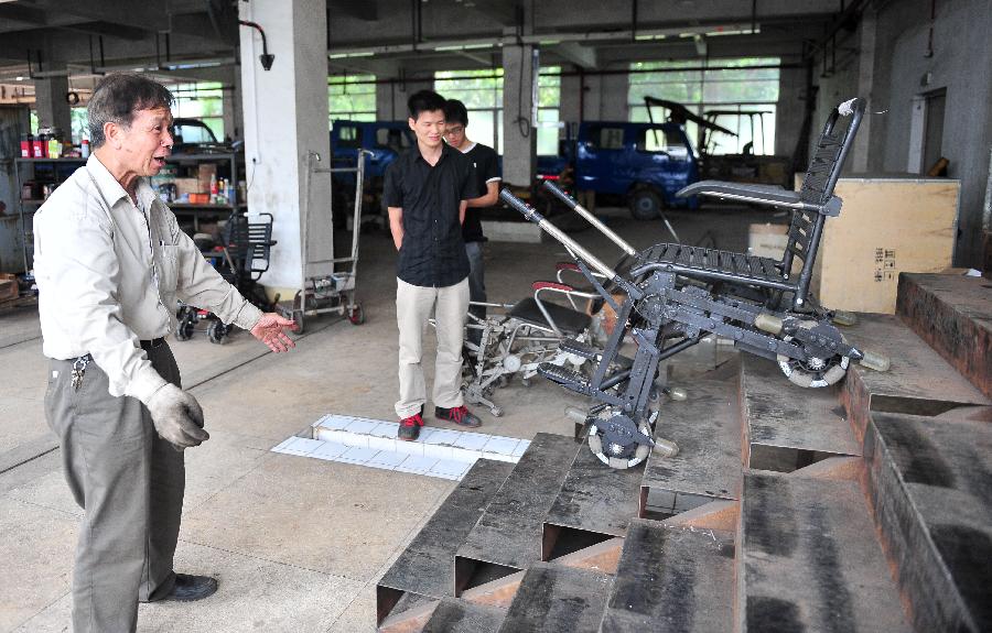 Liu Tie'er (1st L) looks at a wheelchair he invented in a workshop in Guangzhou, capital of south China's Guangdong Province, May 6, 2013. Liu Tie'er, a 71-year-old local resident, invented a wheelchair capable of climbing stairs in an effort to help his disabled wife and many more who are in need. (Xinhua/Lu Hanxin)