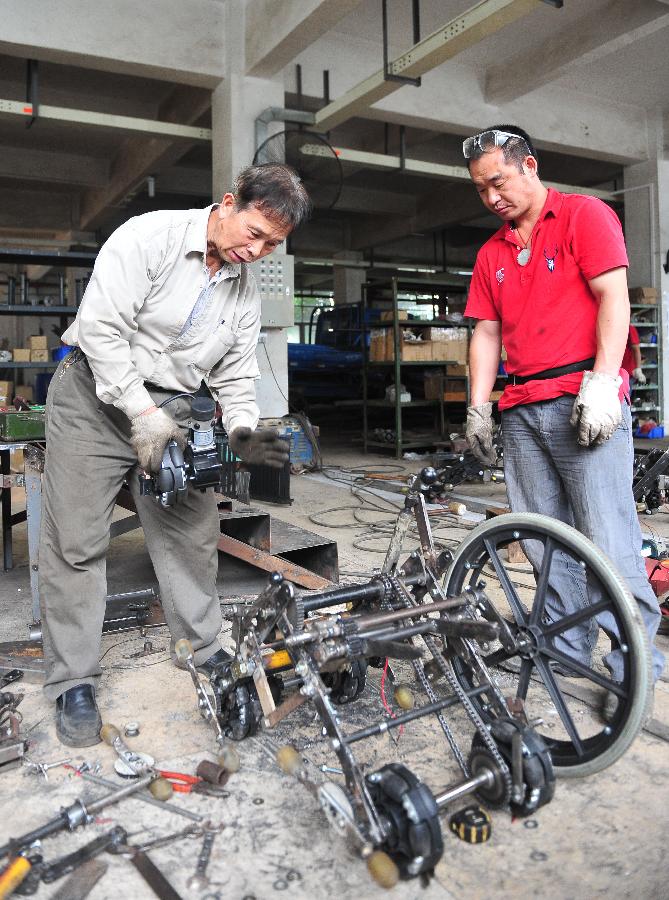 Liu Tie'er (L) installs a wheelchair he invented in a workshop in Guangzhou, capital of south China's Guangdong Province, May 6, 2013. Liu Tie'er, a 71-year-old local resident, invented a wheelchair capable of climbing stairs in an effort to help his disabled wife and many more who are in need. (Xinhua/Lu Hanxin) 