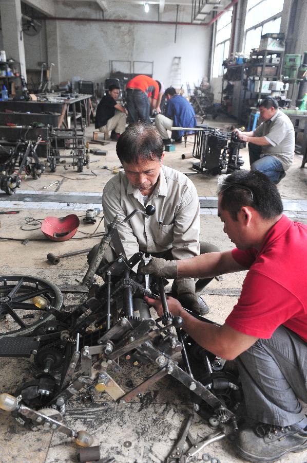 Liu Tie'er (L Front) installs a wheelchair he invented in a workshop in Guangzhou, capital of south China's Guangdong Province, May 6, 2013. Liu Tie'er, a 71-year-old local resident, invented a wheelchair capable of climbing stairs in an effort to help his disabled wife and many more who are in need. (Xinhua/Lu Hanxin) 