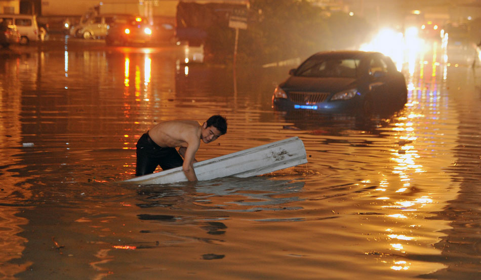 A man tries to put up a sign in the middle of a flooded road to warn passers-by to keep away from the underwater drainage hole after a rainstorm hit Changsha, capital city of central China’s Hunan province, May 7, 2013. (Xinhua/Li Ga)