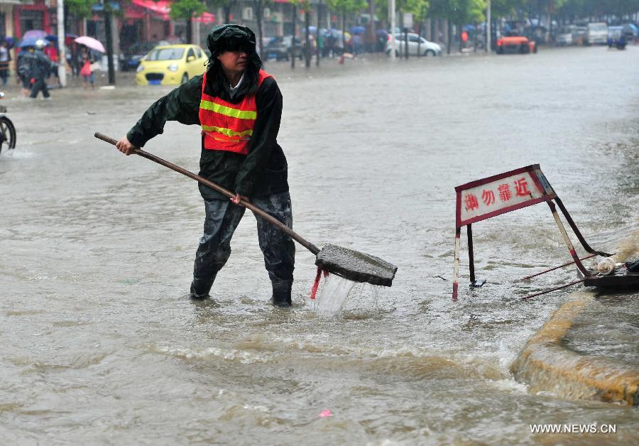 A working staff cleans the debris near a sewer lid on the waterlogged road in Jiujiang City, east China's Jiangxi Province, May 15, 2013. A heavy rainfall hit the city on Wednesday. (Xinhua/Hu Guolin)